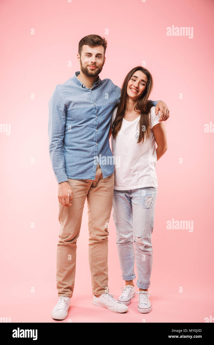 Full length portrait of a smiling young couple hugging while standing ...