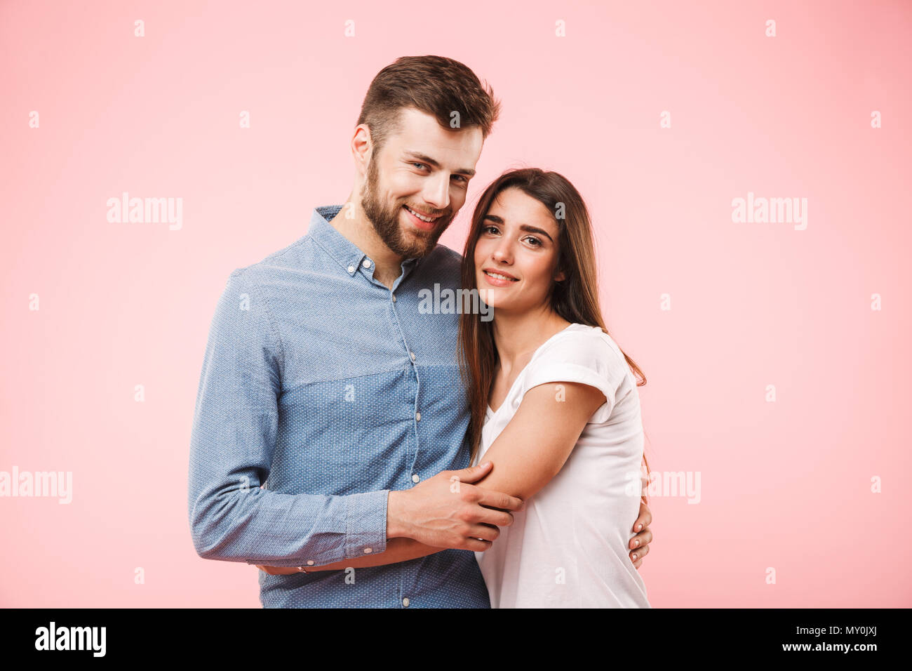 Portrait of a smiling young couple hugging while standing isolated over ...