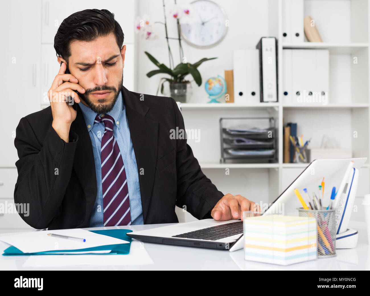 Serious spanish businessman is talking phone with his partner in office. Stock Photo