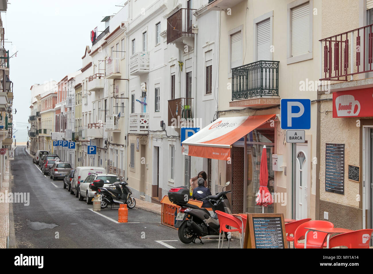 Typical street leading to the beach in Nazare, Portugal. Marked parking spaces are reserved for individual vehicles identified by plates. Stock Photo