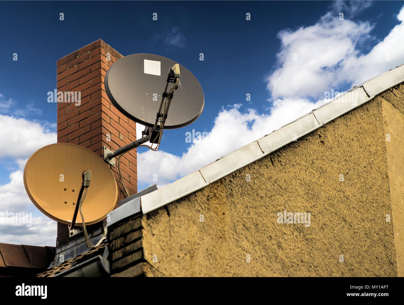 Two satellite dishes in front of a red brick chimney on the sloping roof of a house, germany