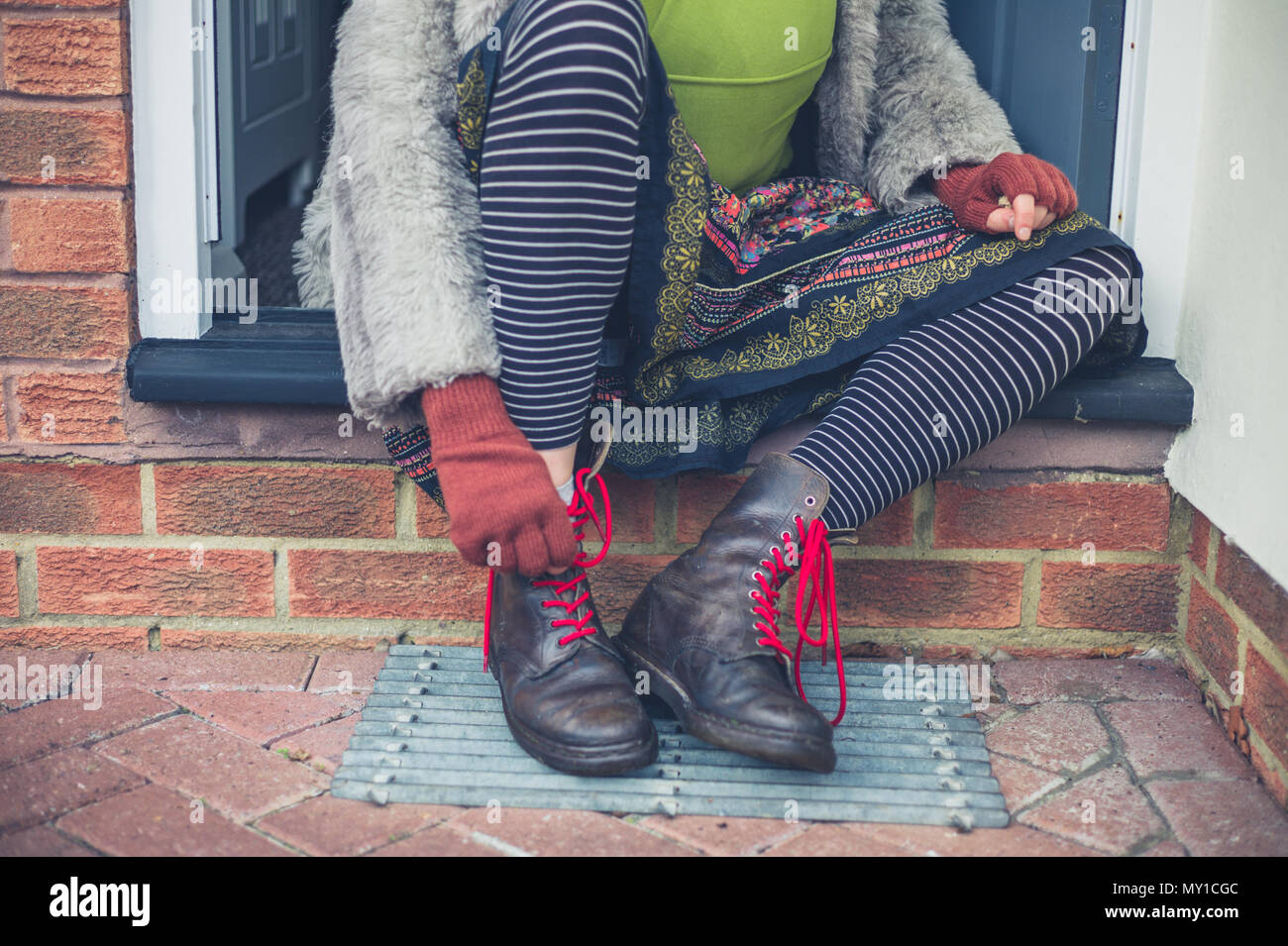 A young woman is tying her boots on a step outside a house Stock Photo