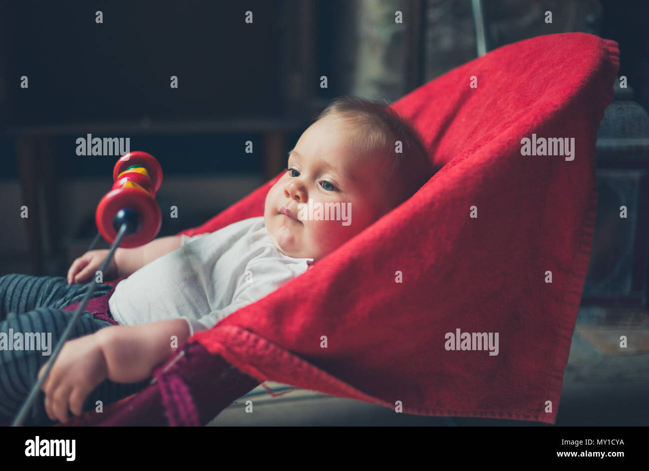 A little baby is sitting in a bouncy chair by the window Stock Photo