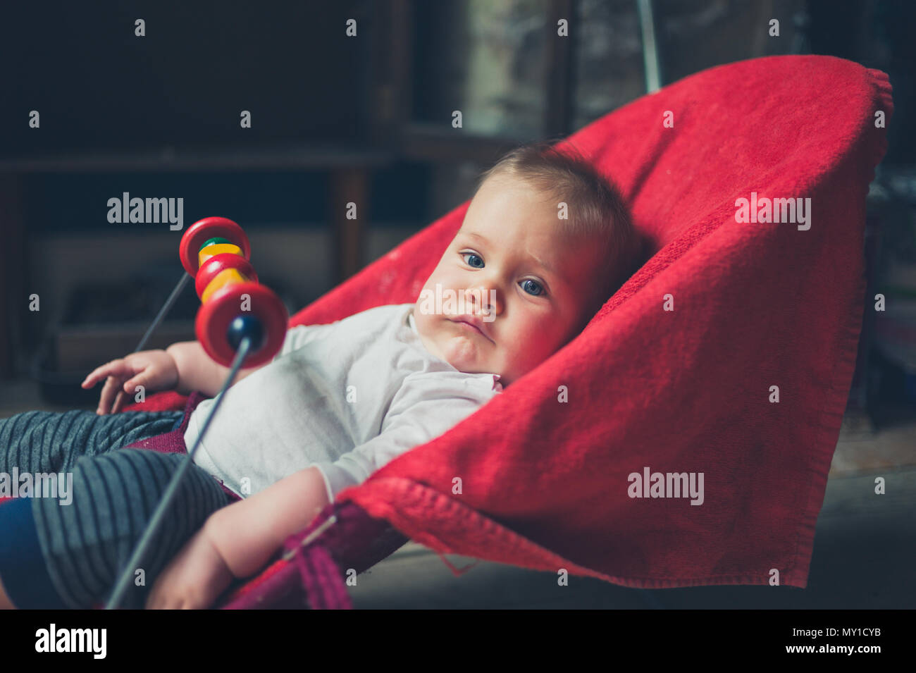 A little baby is sitting in a bouncy chair by the window Stock Photo
