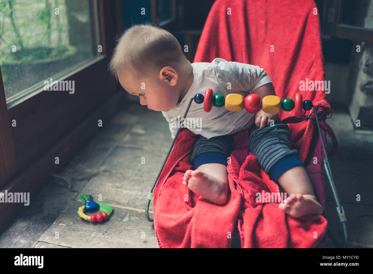 A little baby is sitting in a bouncy chair by the window Stock Photo