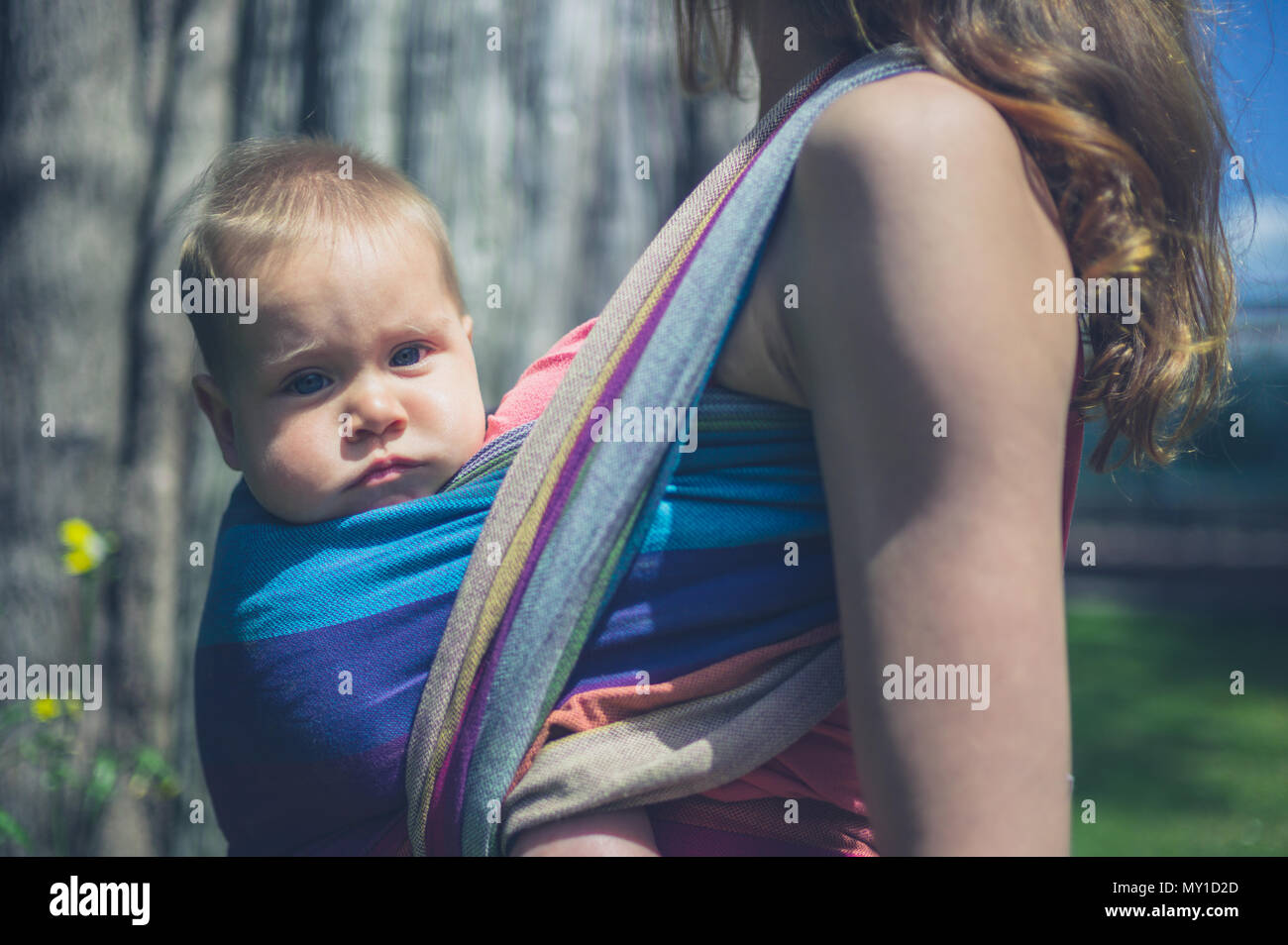 A young mother is standing outside with her baby in a sling Stock Photo