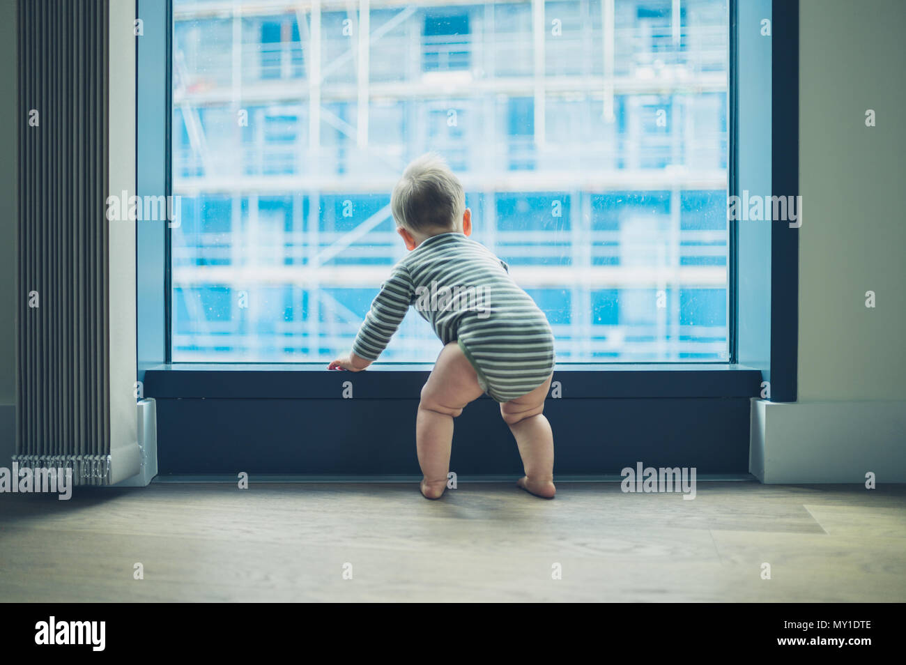 A little baby is looking out the window of a high rise apartment Stock Photo