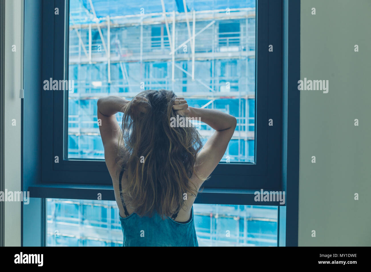 A young woman by the window in a high rise is annoyed by the building ...