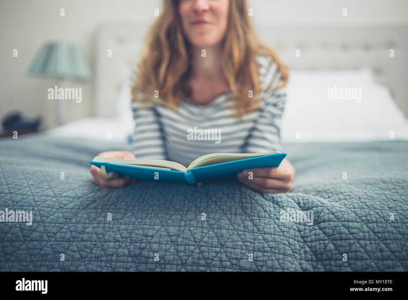 A young woman is lying on a bed and is reading a book Stock Photo