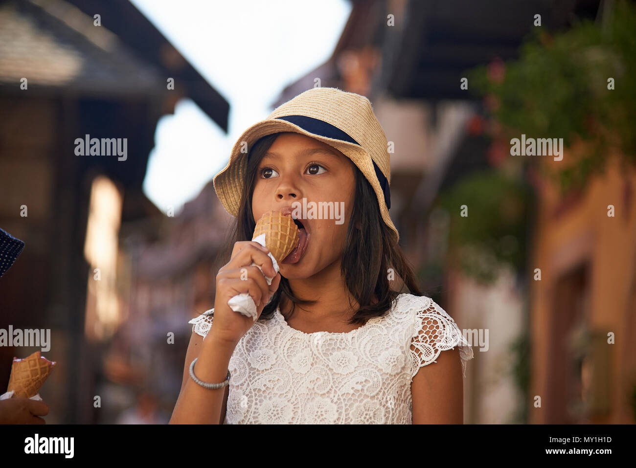 Little cute Asian girl wearing a straw hat eating icecream whilst on holiday in the Alsace region of France in summer sunshine on a hot day Stock Photo
