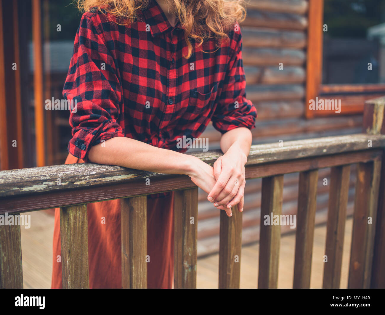 A young woman is relaxing on the porch of a log cabin in the country ...