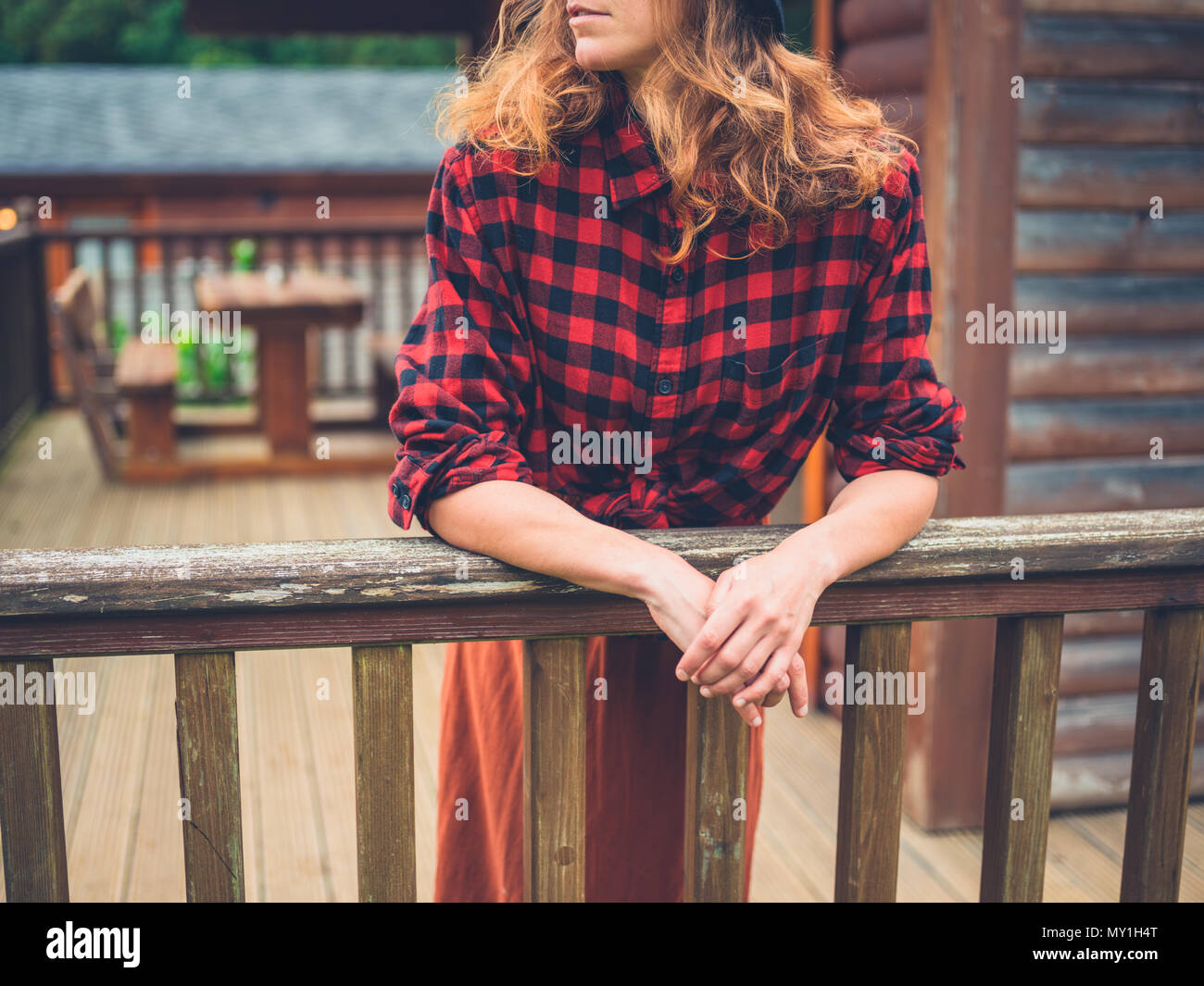 A young woman is relaxing on the porch of a log cabin in the country ...