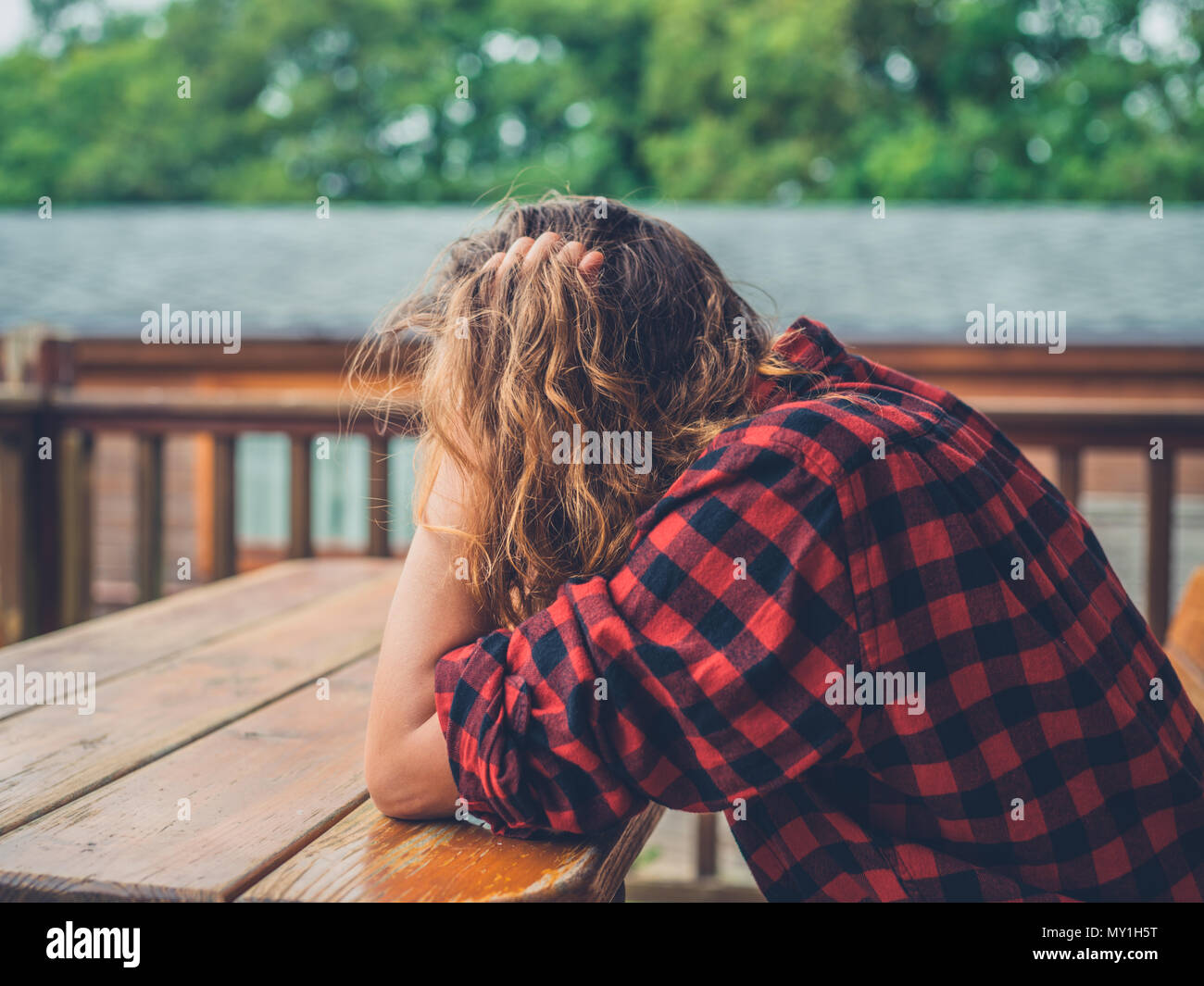 A sad and tired young woman is sitting on the porch of a log cabin ...