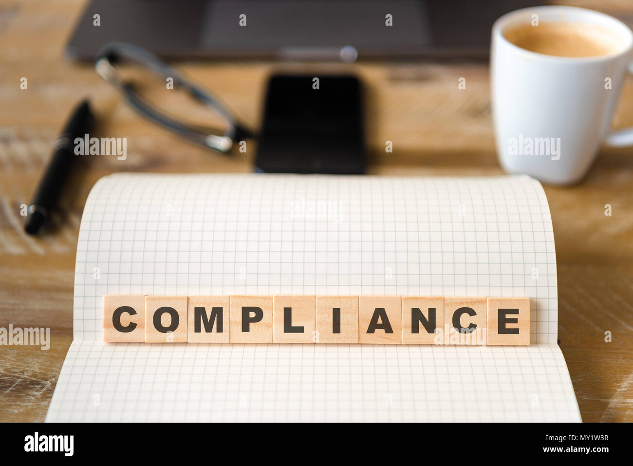 Closeup on notebook over wood table background, focus on wooden blocks with letters making Compliance text. Stock Photo