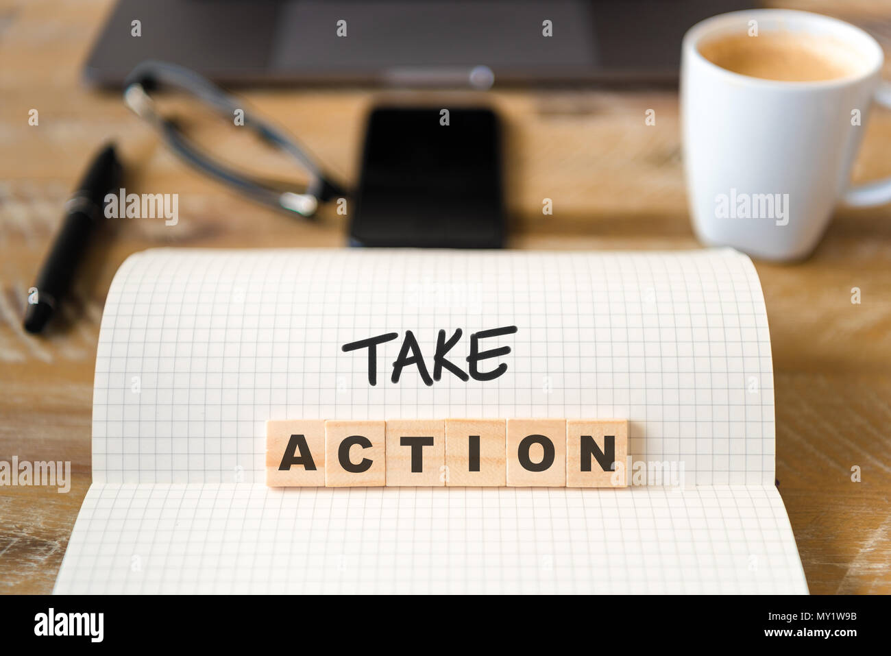 Closeup on notebook over wood table background, focus on wooden blocks with letters making Take Action text. Stock Photo