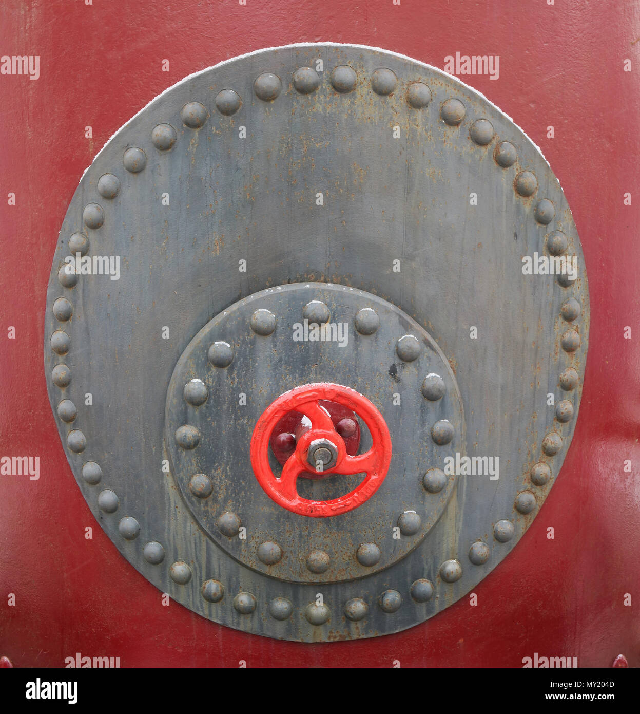 Gray and red steel sheets are joined together by rivets. The mechanical valve wheel is installed. Background of steam punk vintage style. Cold snowy s Stock Photo