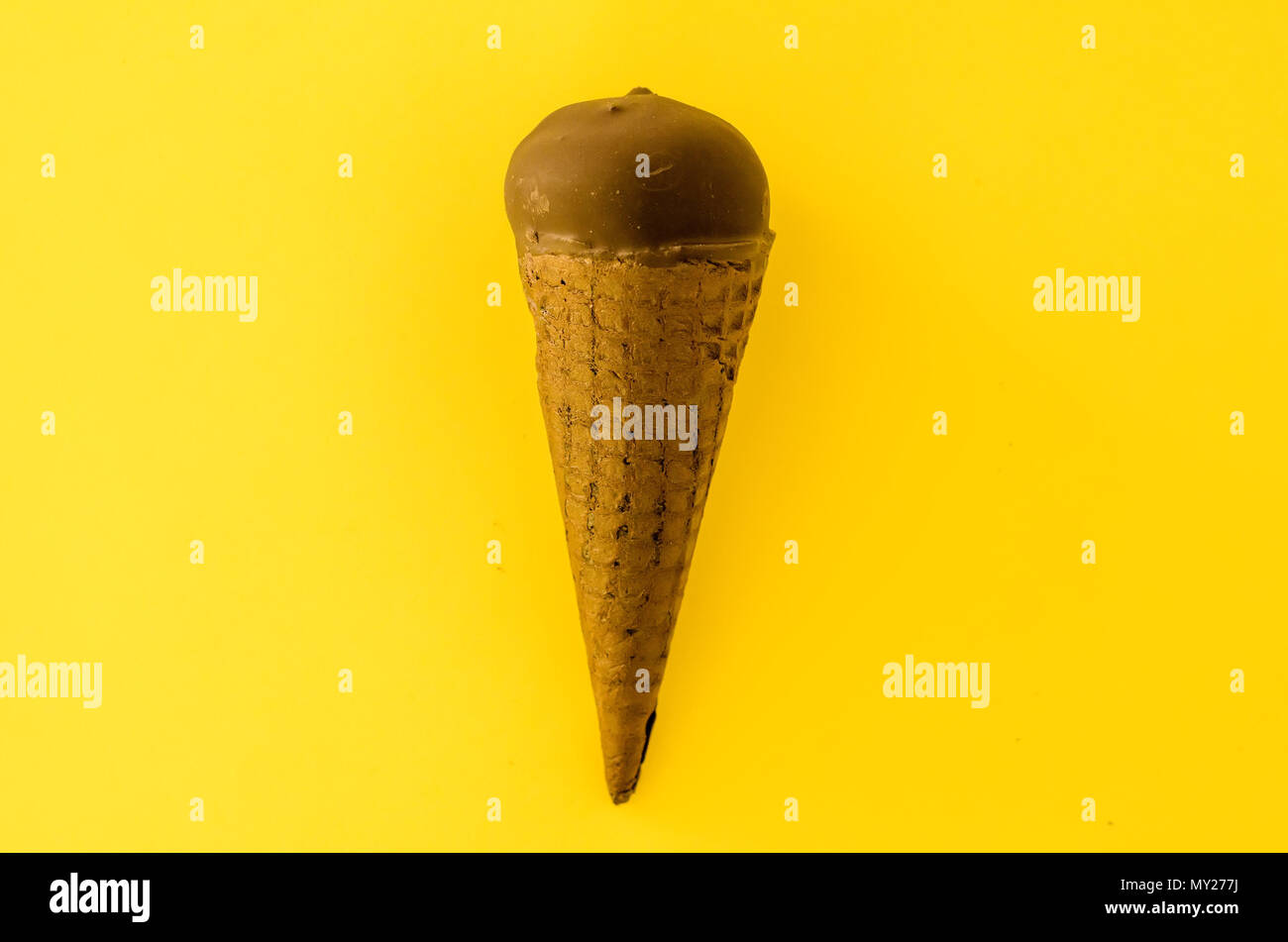 Vanilla ice cream with cranberry jam in a sugar cone dipped in chocolate on yellow background.Pastel colour.Cool off in the hot summer.Copy space left Stock Photo