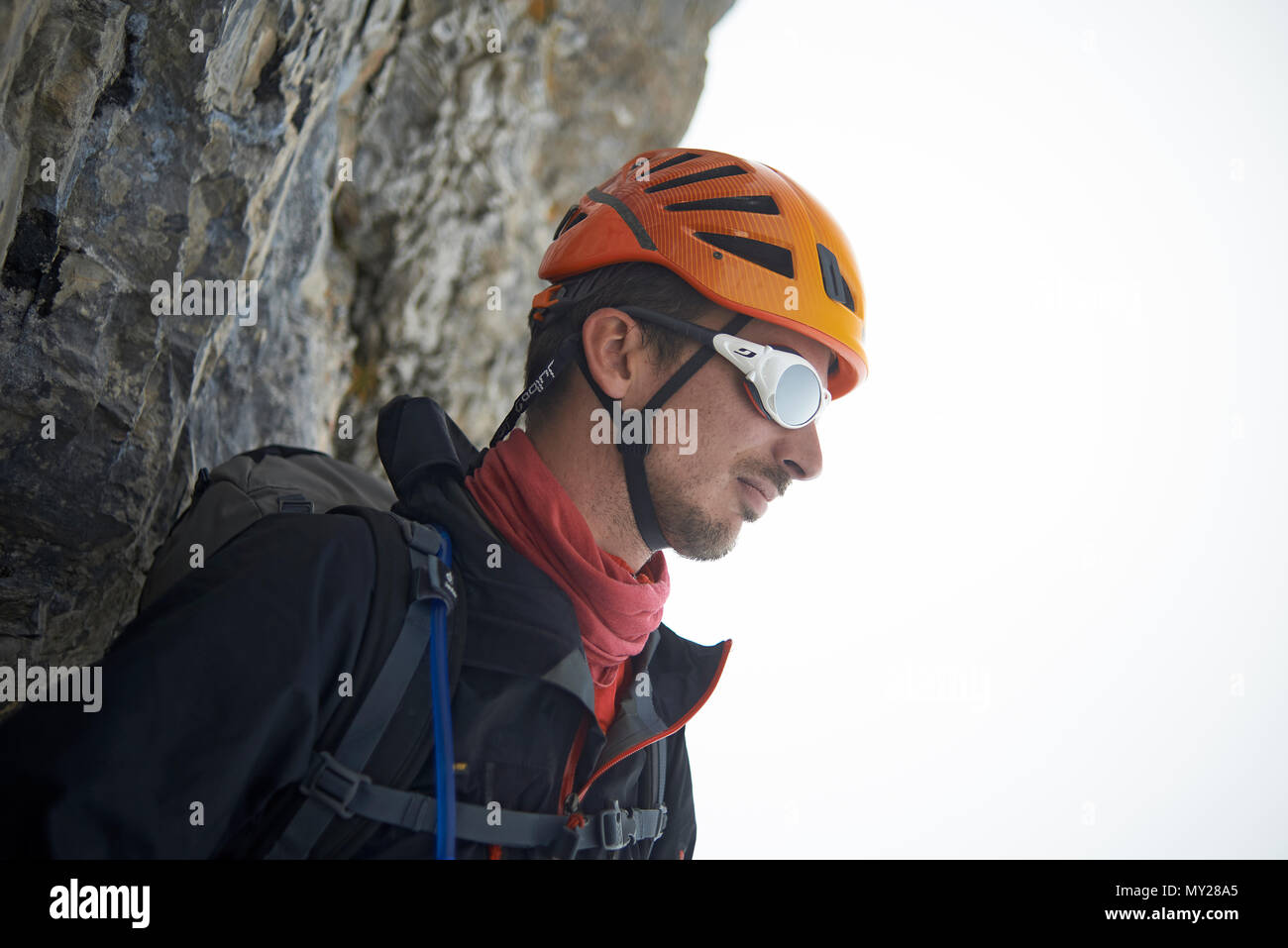 Mountaineer standing on a rock in climbing gear looking out into the distance over the mountains Stock Photo