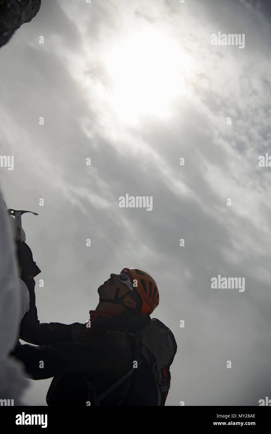 Mountaineer climbing a snowy rock using a pick hammer to reach the top of a mountain at high altitude in the Swiss Alps reaching new goals Stock Photo