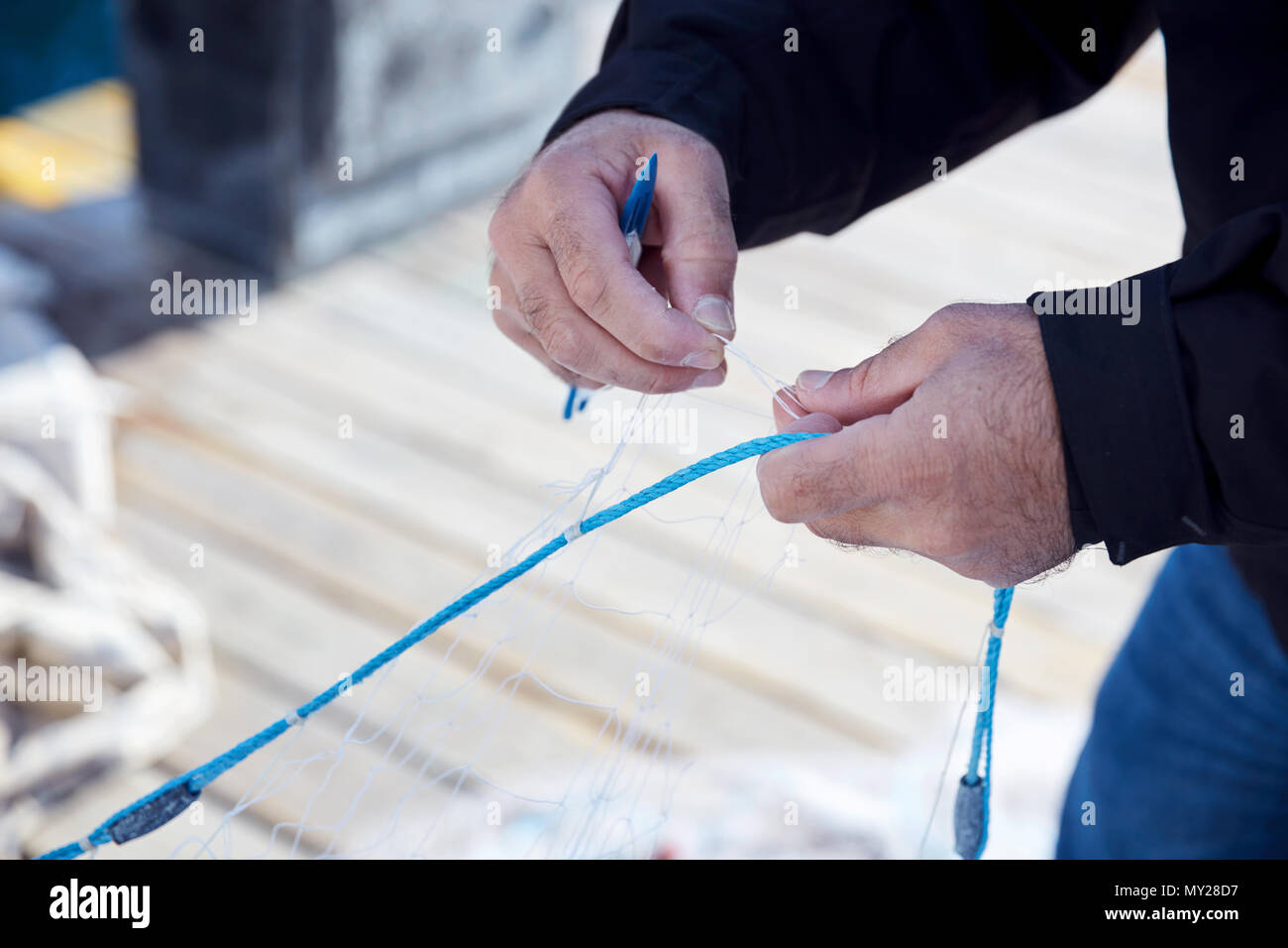 Fisherman repairing a fishing net with a net needle on the harbor Stock