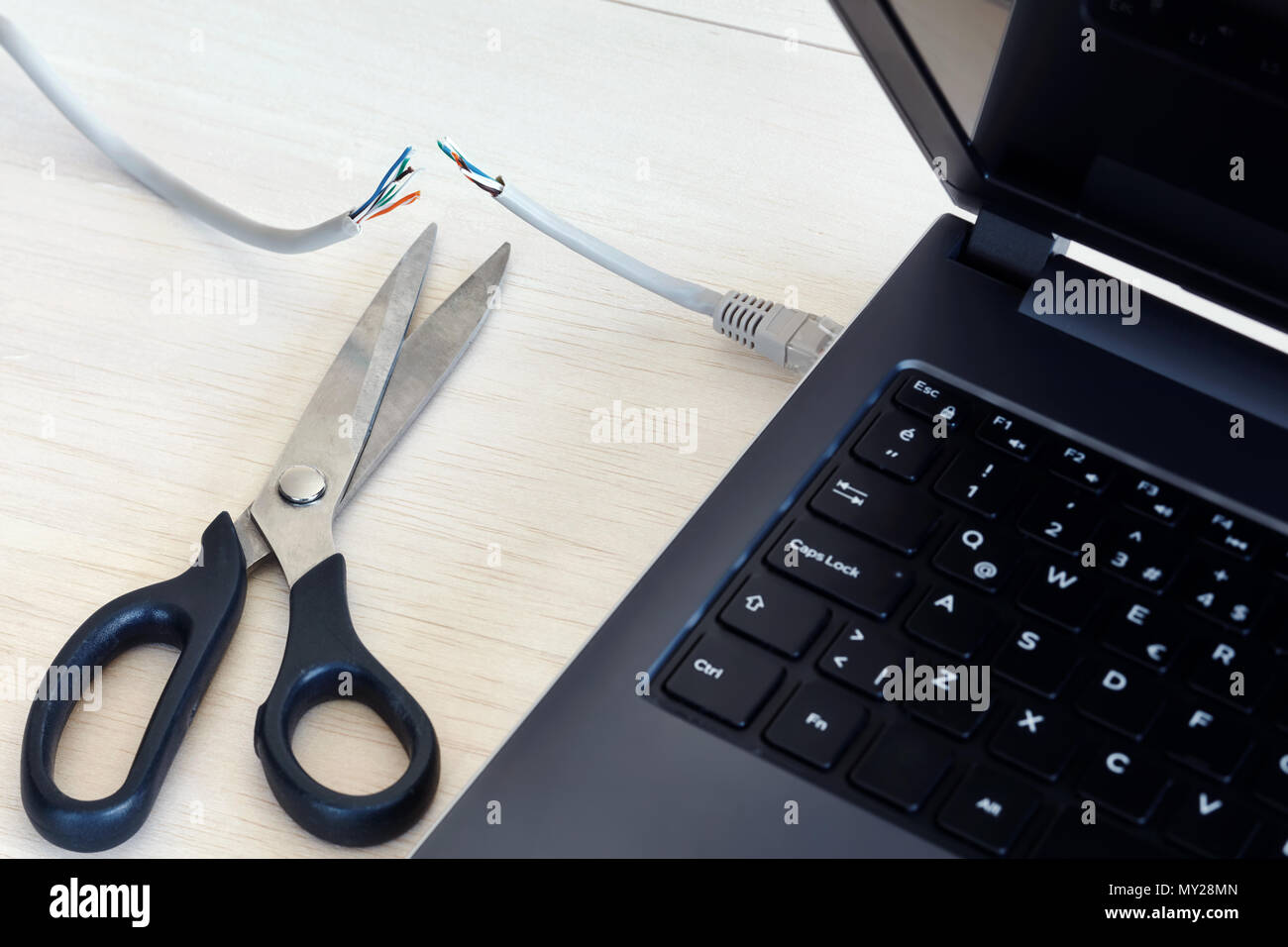 Internet cable connected to a laptop computer cut by a scissors. Concept of internet ban, cencorship and interruption. Stock Photo