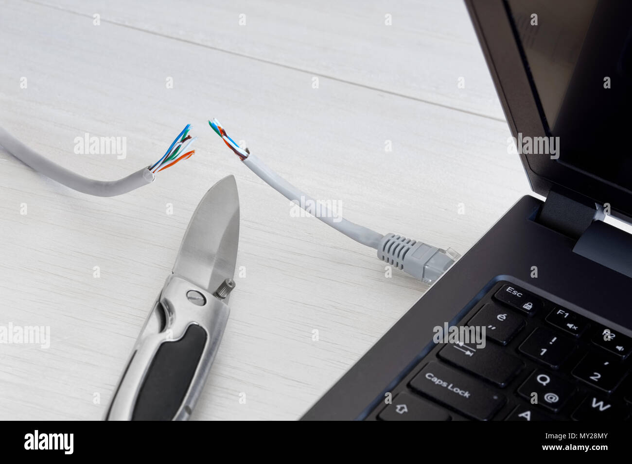Internet cable connected to a laptop computer cut by a pocket knife. Concept of internet ban, cencorship and interruption. Stock Photo