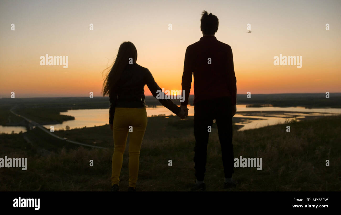 Loving young couple holding hands looking each other at amazing sunset ...