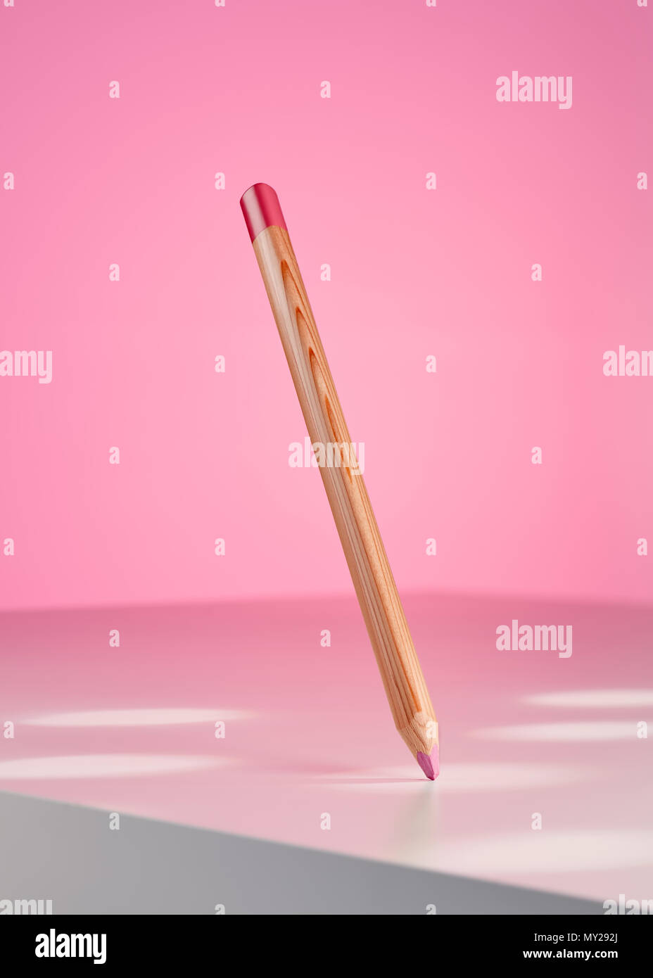 Pink colored pencil hanging on the air and pointing out a spot on the white table Stock Photo