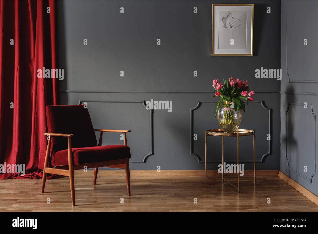 Simple waiting room interior with a single red armchair standing against dark gray wall with molding next to a golden table with pink flowers. Real ph Stock Photo