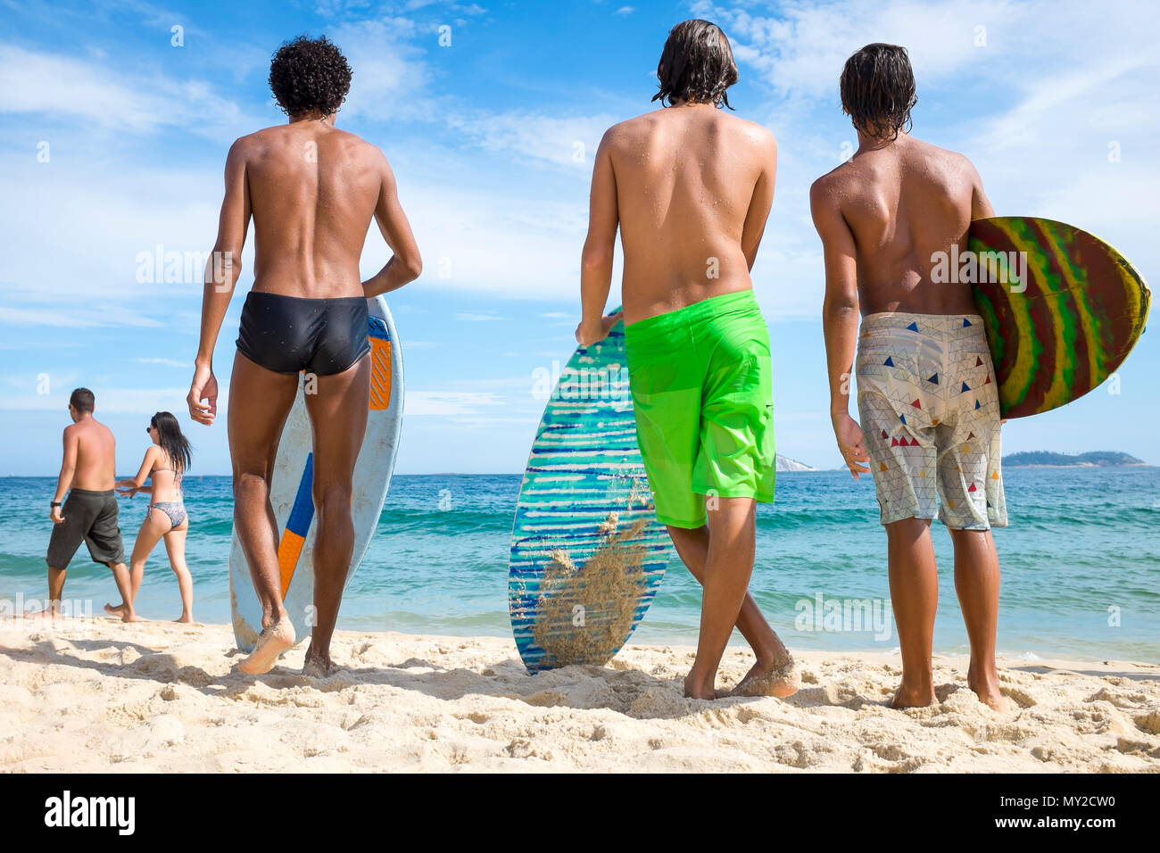 Young Brazilian men stand with skimboards on the shore of Ipanema Beach in Rio de Janeiro, Brazil Stock Photo