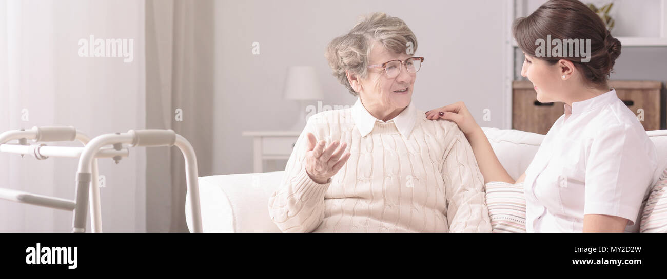 Panorama of a senior woman talking to a young, female caregiver in a private rehabilitation center Stock Photo
