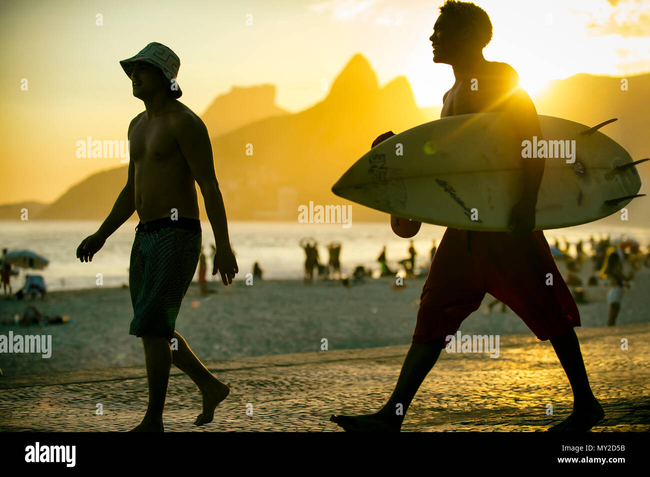 RIO DE JANEIRO - MARCH 20, 2017: Sunset silhouettes of two young surfers with surfboard at Arpoador, Ipanema with two brothers mountain in background Stock Photo