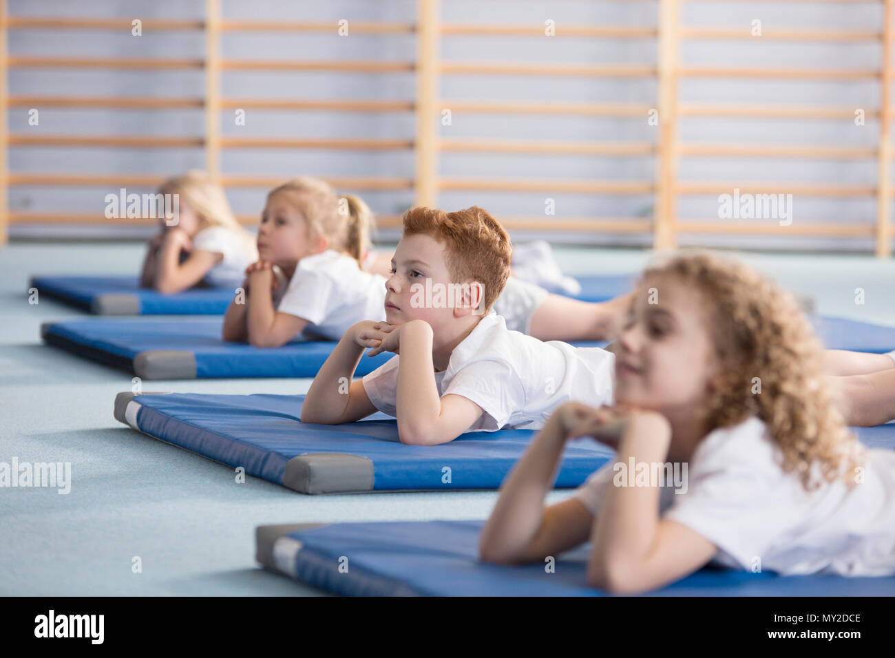 Boy relaxing on a blue mat with friends in a primary school Stock Photo