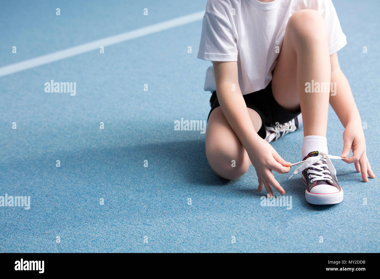 Close-up of kid tying a shoe on blue floor at the gym Stock Photo