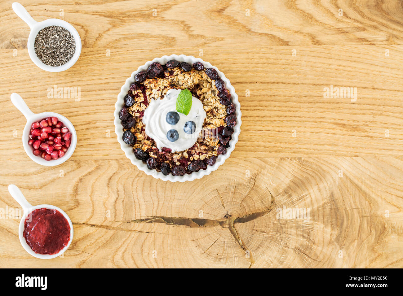 Top view of breakfast granola with fruit, cups with pomegranate, jam and chia seeds and place for your ingredients on a wooden kitchen table Stock Photo