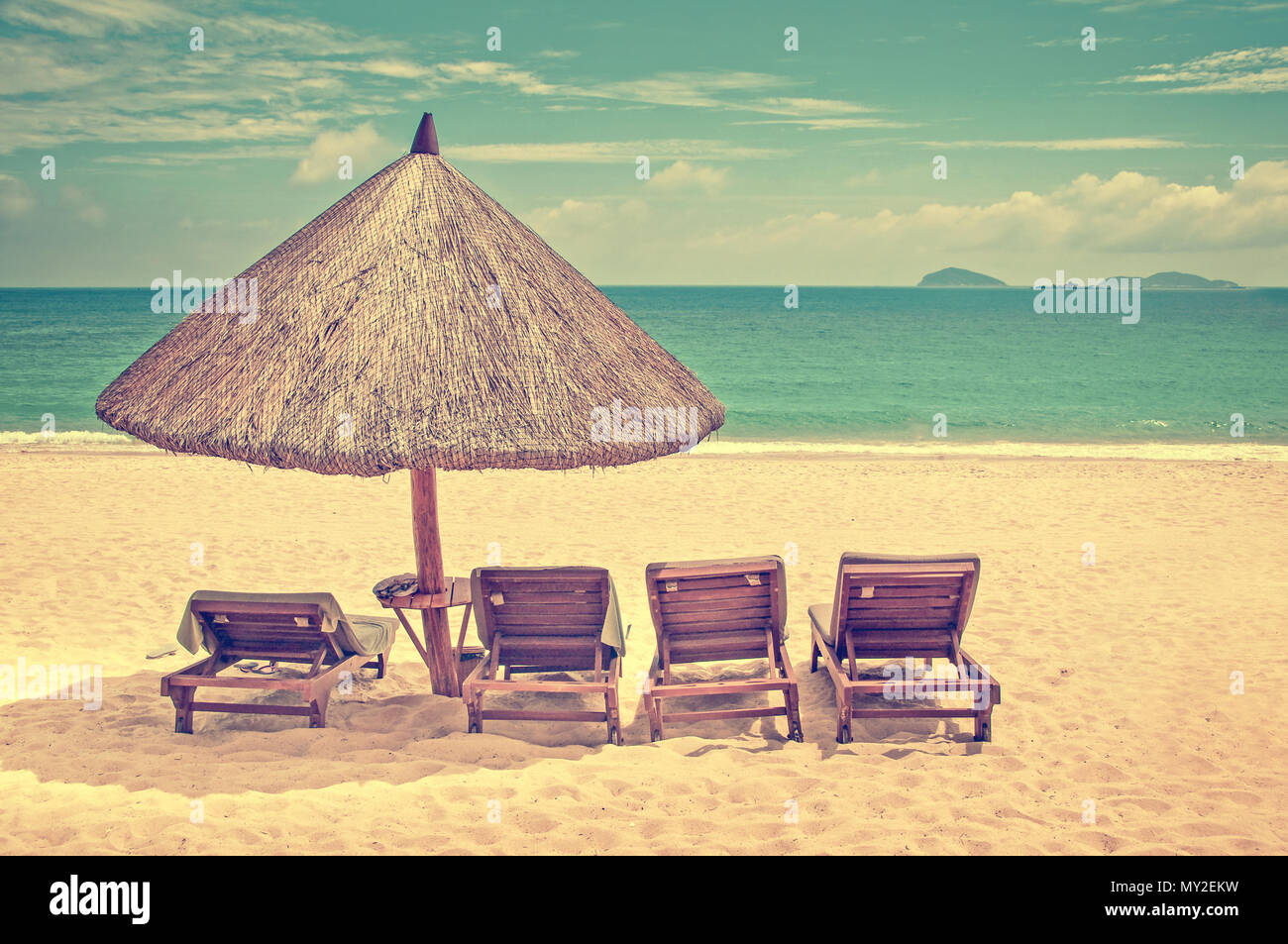 Straw beach umbrella and wooden reclining chairs on a perfect beach