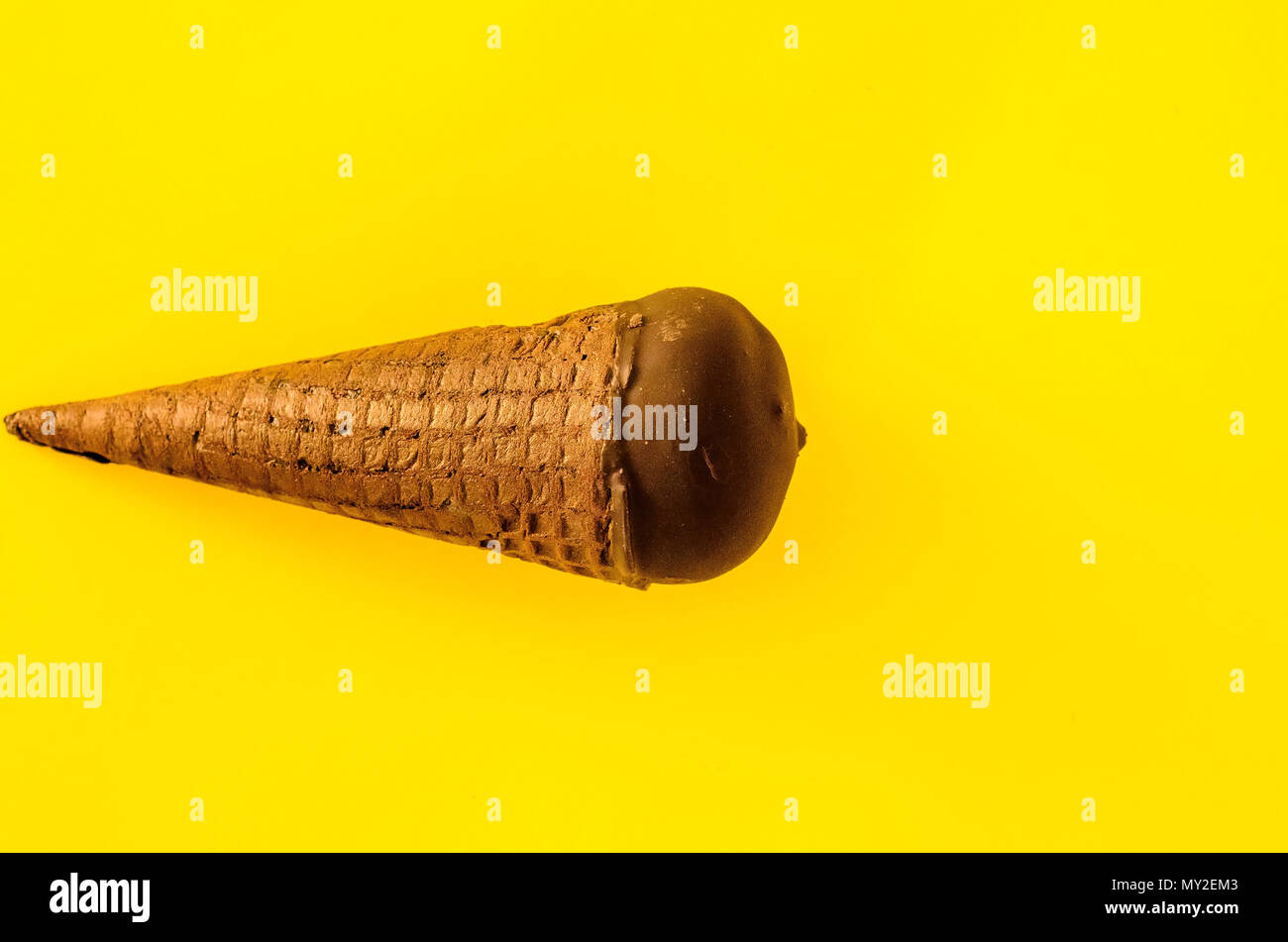 Vanilla ice cream with cranberry jam in a sugar cone dipped in chocolate on yellow background.Pastel colour.Cool off in the hot summer.Copy space righ Stock Photo