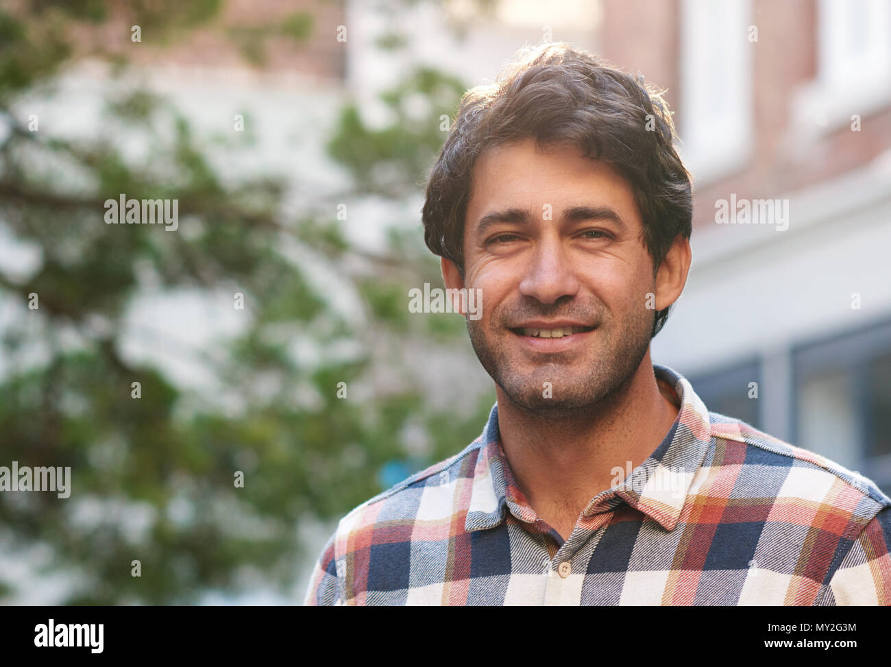 Closeup portrait of a casually dressed handsome man smiling while standing by himself on a street in the city on a sunny afternoon Stock Photo