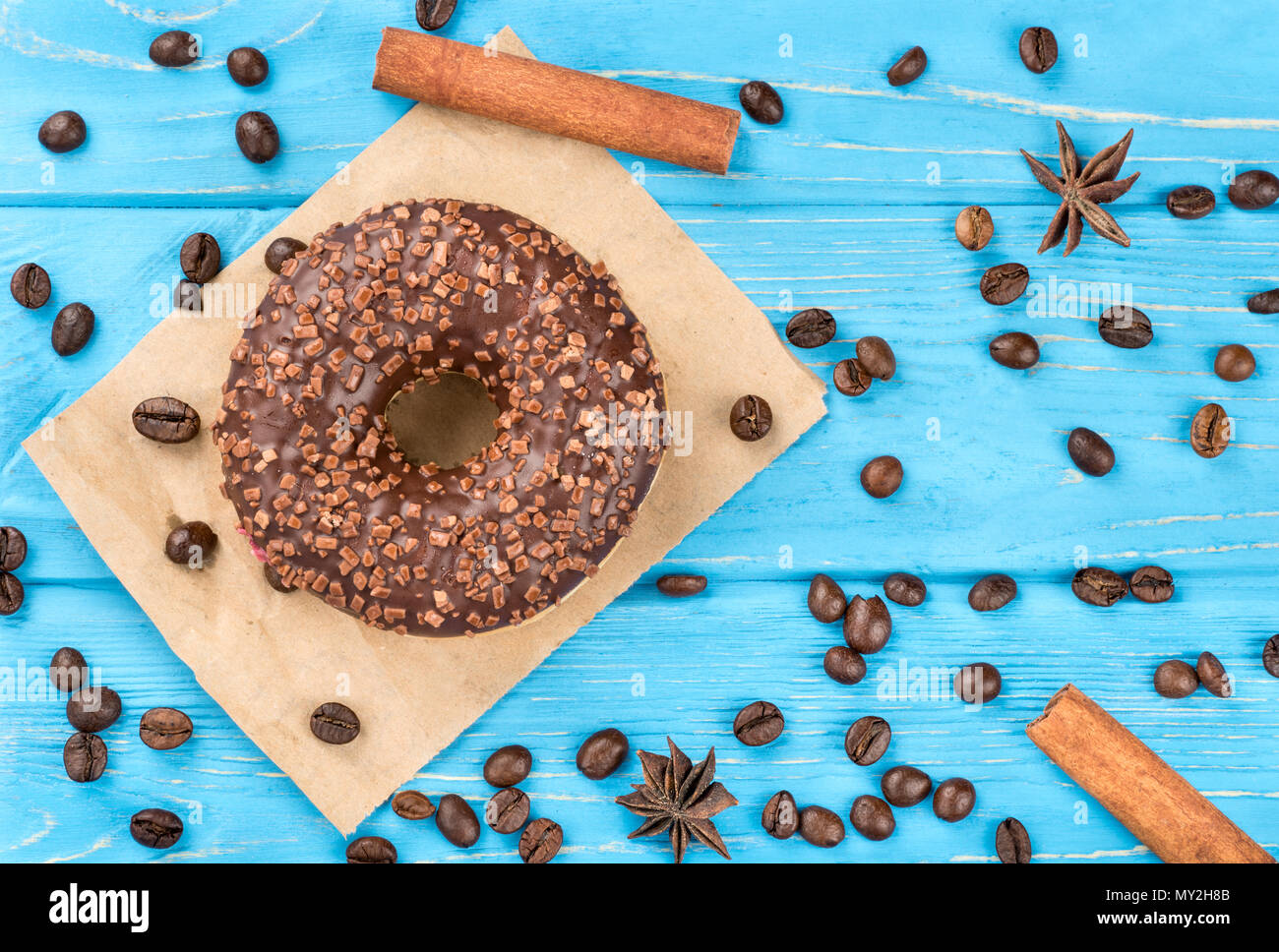 Chocolate donut with coffee beans scattered on a blue table, top view Stock Photo