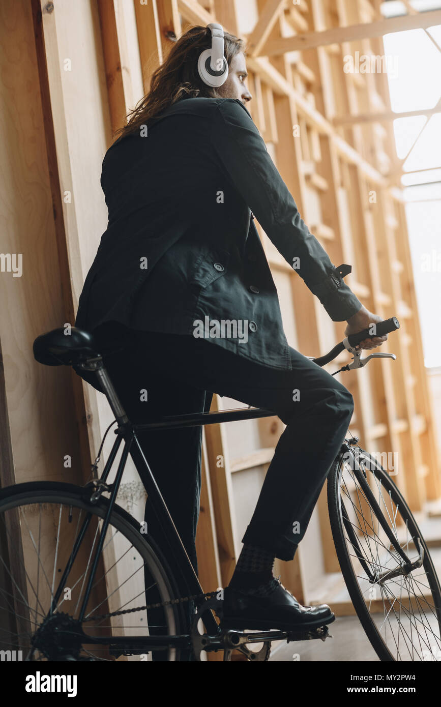 Back view of stylish young man in headphones riding bicycle and looking