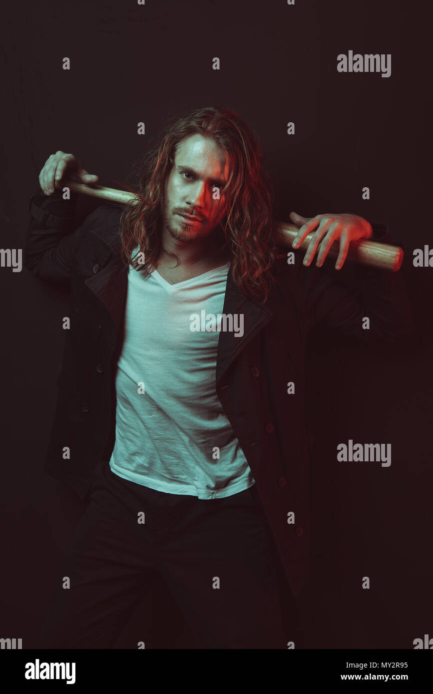 Portrait of serious stylish long haired man holding baseball bat on