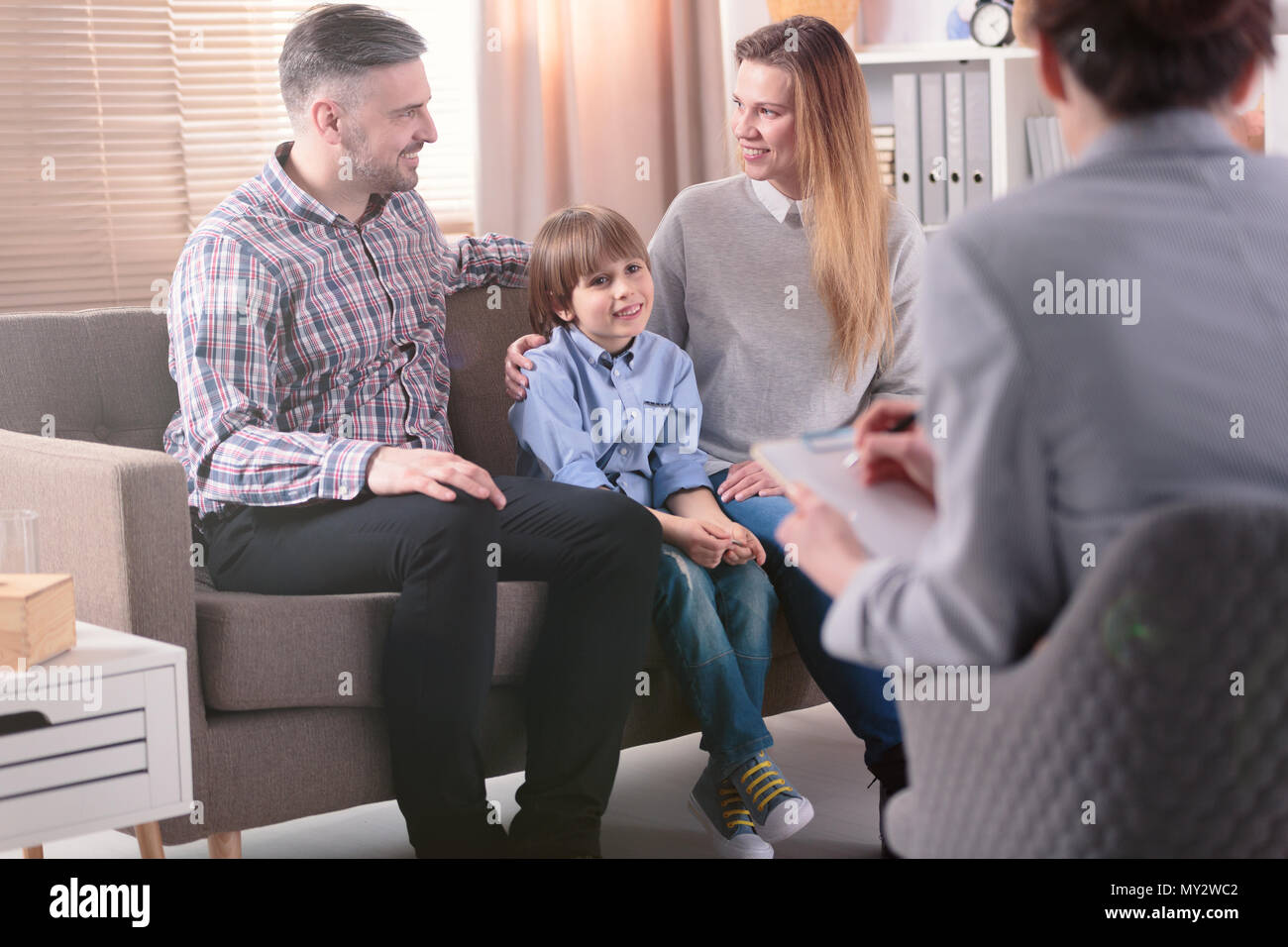 Rear view at successful female psychotherapist helping young family with a child to solve problems in relationship. Happy family in the background Stock Photo
