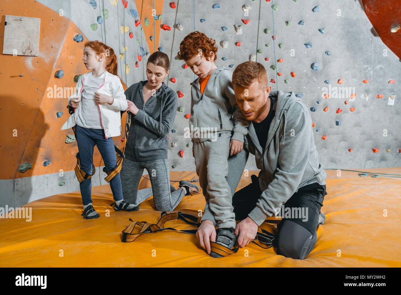 Parents securing their children in harnesses for climbing a wall with