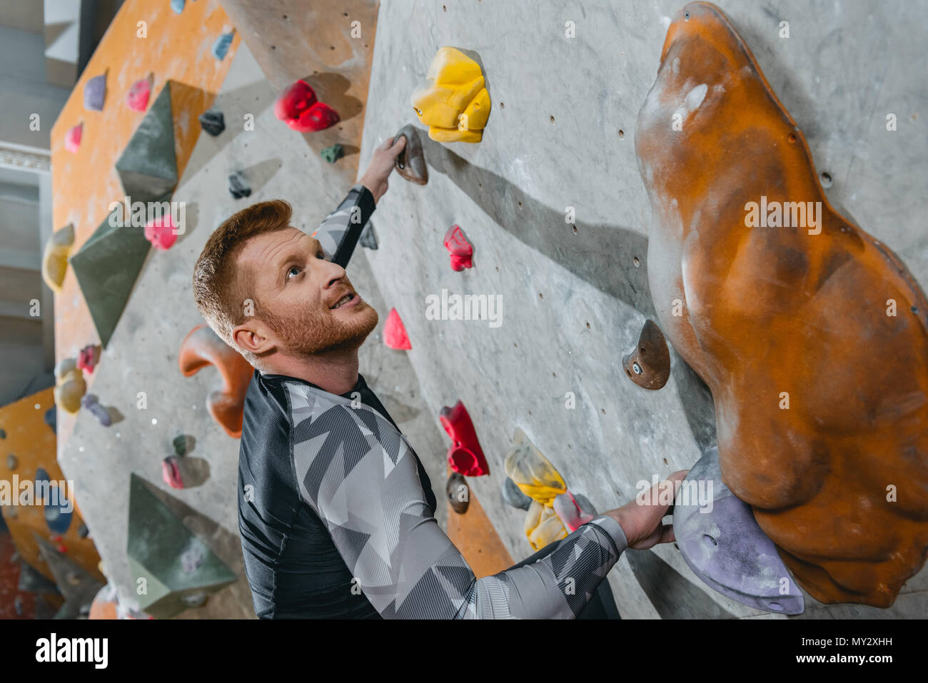 halflength shot of young man in sportive attire climbing a wall with