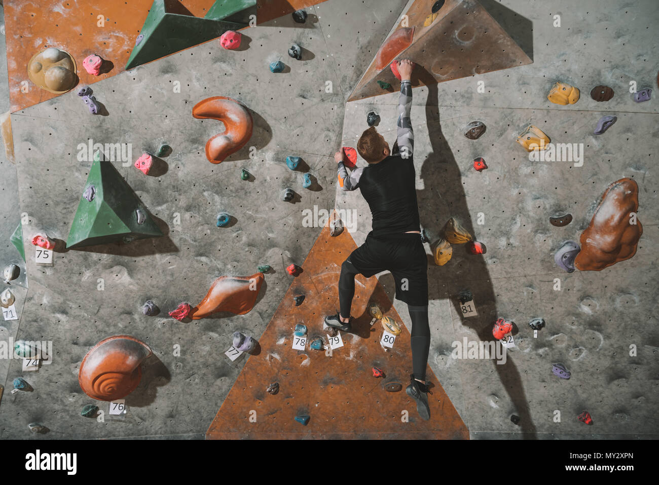 Rear view shot of young man in sport attire climbing a wall with grips at gym Stock Photo Alamy