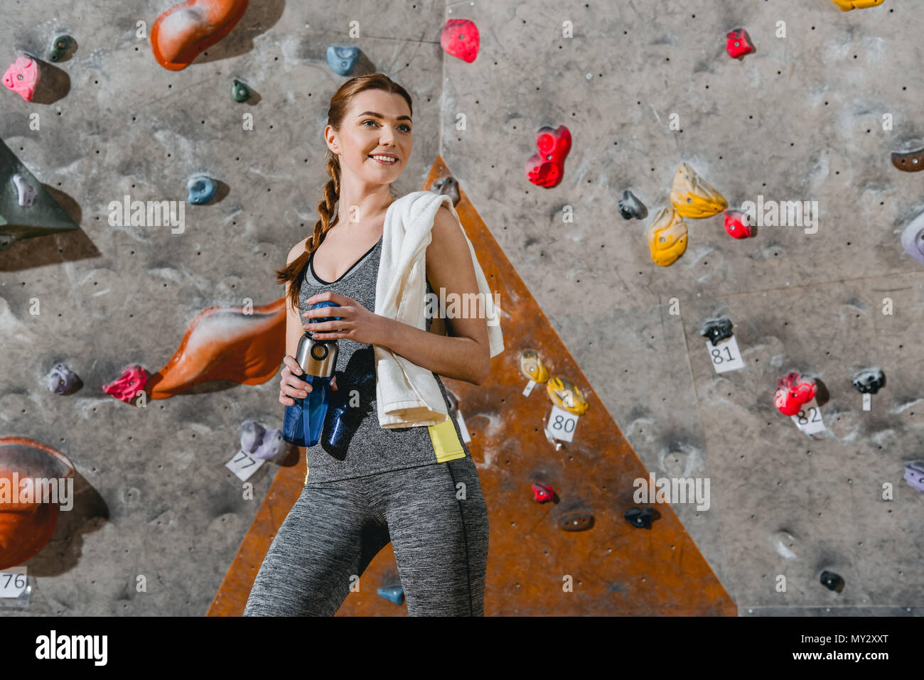 Halflength shot of a young woman in sportive attire posing in front of climbing wall Stock