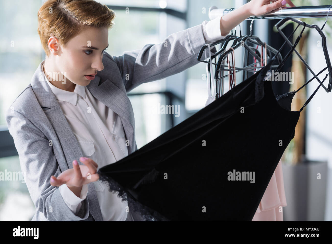 serious fashion designer examining quality of clothing on hangers Stock
