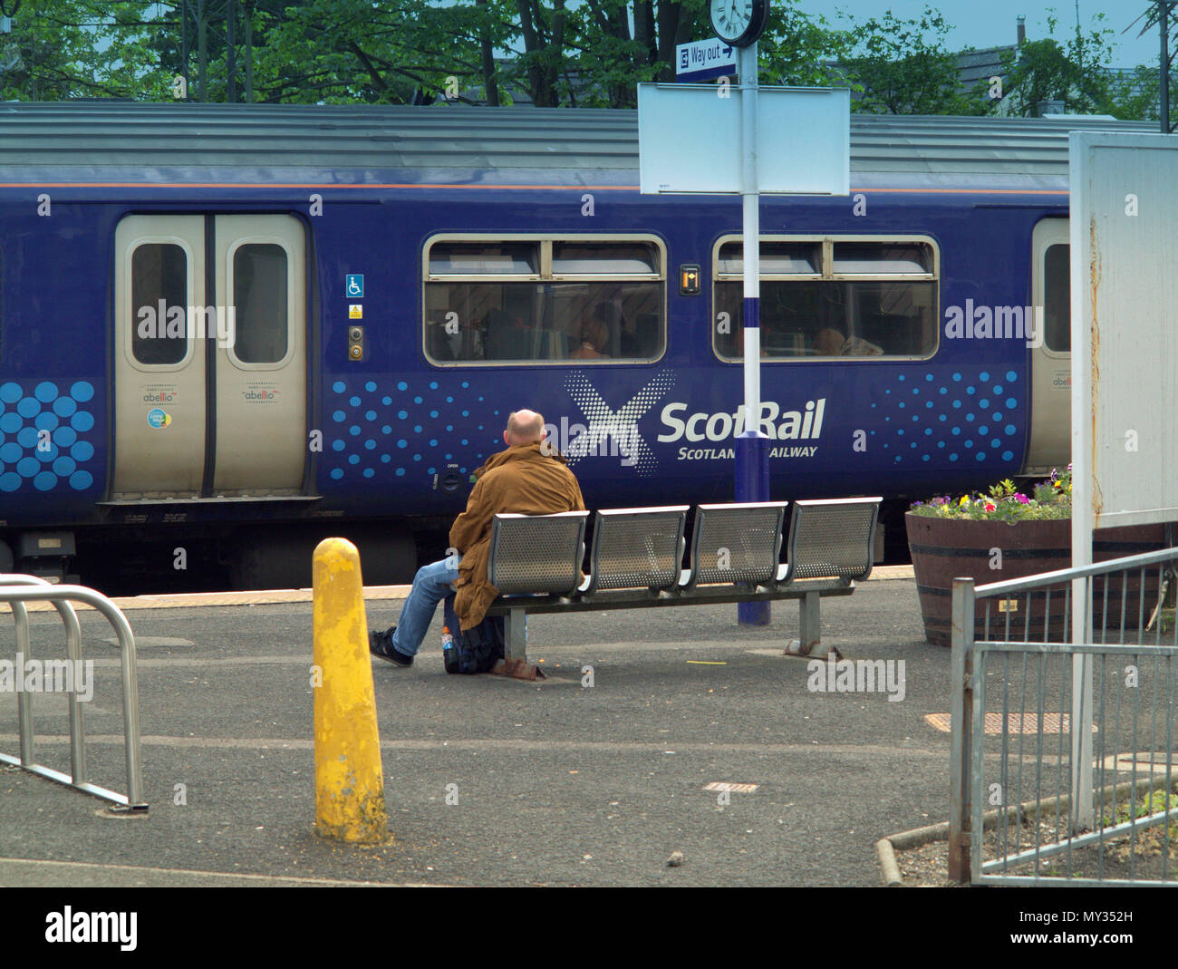 train scotrail commuter passenger sitting on bench yellow phallic symbol bollard drumchapel railway station Stock Photo