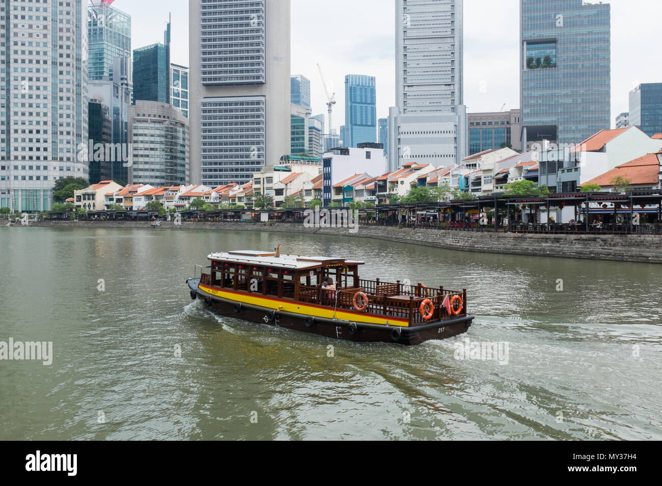 Old Singapore Bumboat taking tourists on a cruise on the Singapore River passing Boat Quay Stock Photo