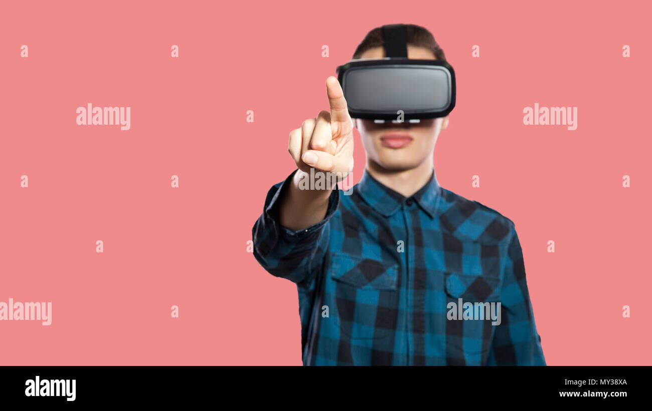 young man with vr headset touching screen. studio shot, isolated on pink background. Stock Photo